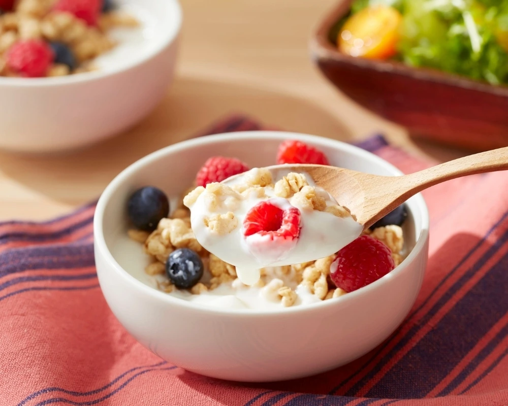 A small bowl of yogurt with granola, raspberries and blueberries.